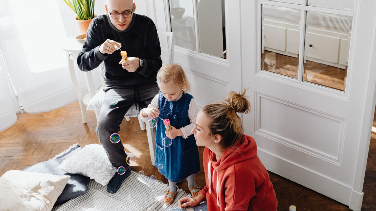 A family bonding while blowing bubbles together indoors, capturing a joyful moment.